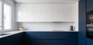 Diseño de cocina moderna en L con armarios azul marino mate y blancos brillantes sin tiradores. Una de las principales tendencias de cocinas 2026. Encimera blanca y placa de inducción.