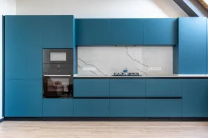Diseño moderno mostrando muebles de cocina sin tiradores en color azul mate, con sistema de apertura de perfil Gola negro y encimera blanca veteada.