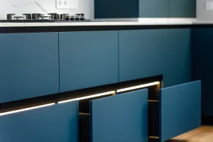 Detalle de las tendencias cocinas 2026 mostrando muebles lisos en azul oscuro mate, diseño sin tiradores e iluminación LED integrada en los cajones.